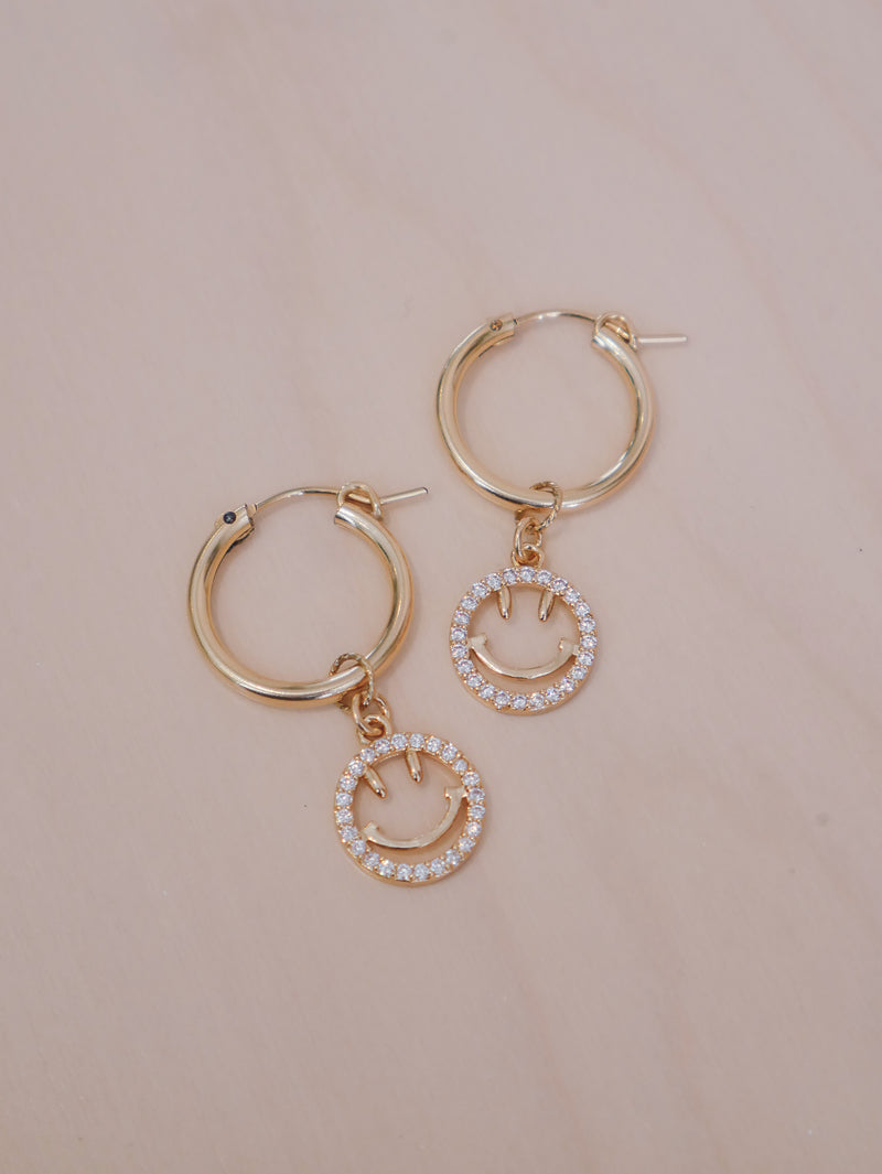 Add a fun twist to any look with our Gelos Hoops earrings. Crafted with 14k gold-filled hoops, the earrings feature a cheerful smiley face that adds a happy sparkle to any outfit.   Gold-filled hoops 19mm (M) - as shown 14k plated and zircon smileys 4cm total length  Smileys are removable to wear hoops separately Suitable for sensitive skin  Comes with cotton pouch and cleaning cloth