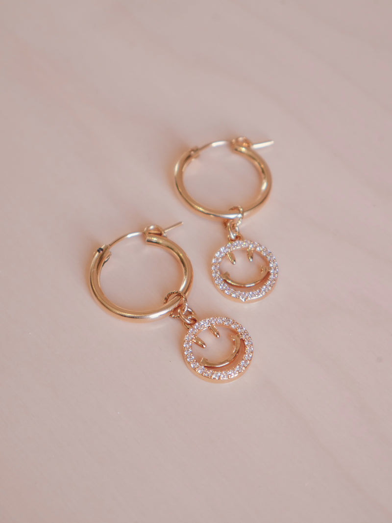 Add a fun twist to any look with our Gelos Hoops earrings. Crafted with 14k gold-filled hoops, the earrings feature a cheerful smiley face that adds a happy sparkle to any outfit.   Gold-filled hoops 19mm (M) - as shown 14k plated and zircon smileys 4cm total length  Smileys are removable to wear hoops separately Suitable for sensitive skin  Comes with cotton pouch and cleaning cloth